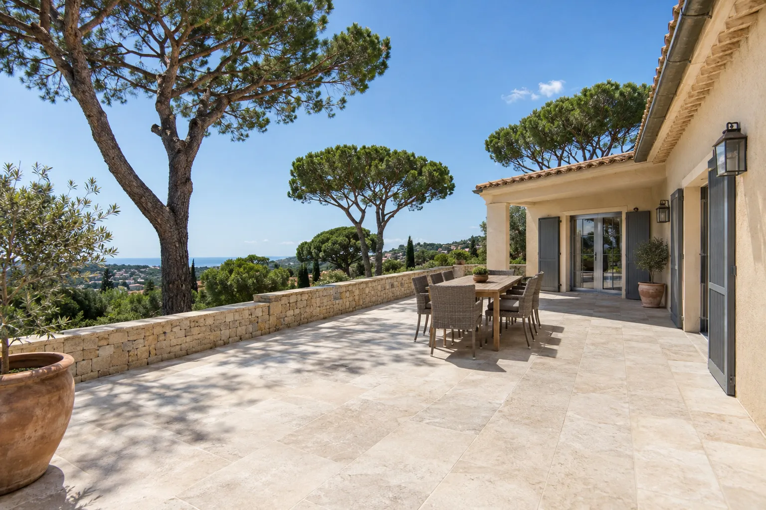 Une terrasse de villa marseillaise carrelée en grès cérame antidérapant, légère pente vers le bord, mur de pierre en fond.