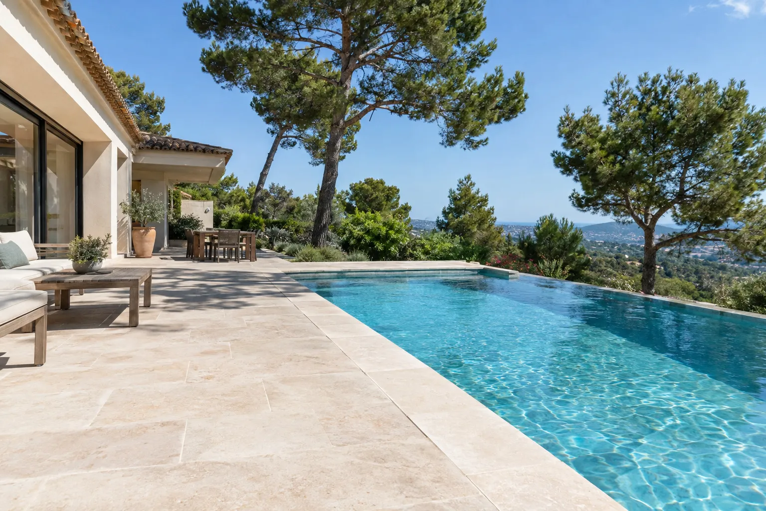 Terrasse de villa terminée en dalles de pierre naturelle claire, en bord de piscine, sous les pins.